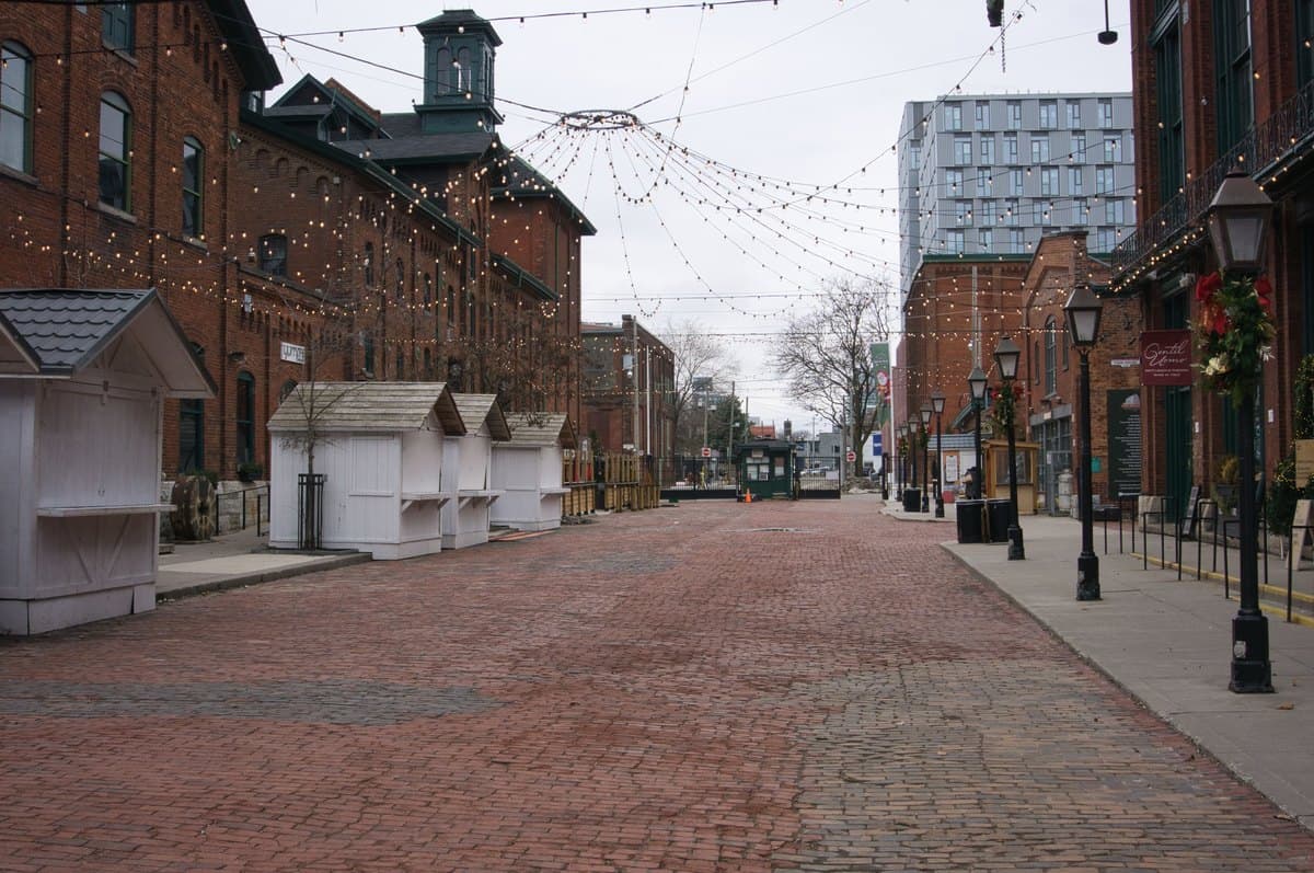 Brick-paved Trinity Street in Toronto's Distillery District, with red-brick buildings, overhead lights and closed seasonal stalls