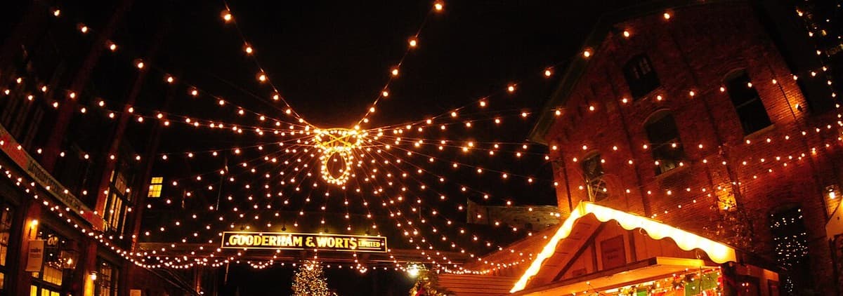 Strings of Christmas lights above the Gooderham and Worts sign and wooden market-stall roofs in Toronto's Distillery District