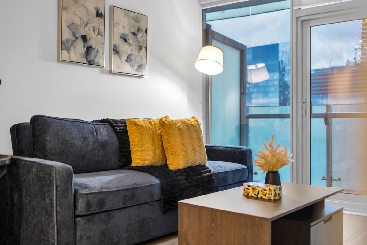Blue sofa with yellow cushions, wooden coffee table and balcony doors in a York one-bedroom plus den with sofa bed