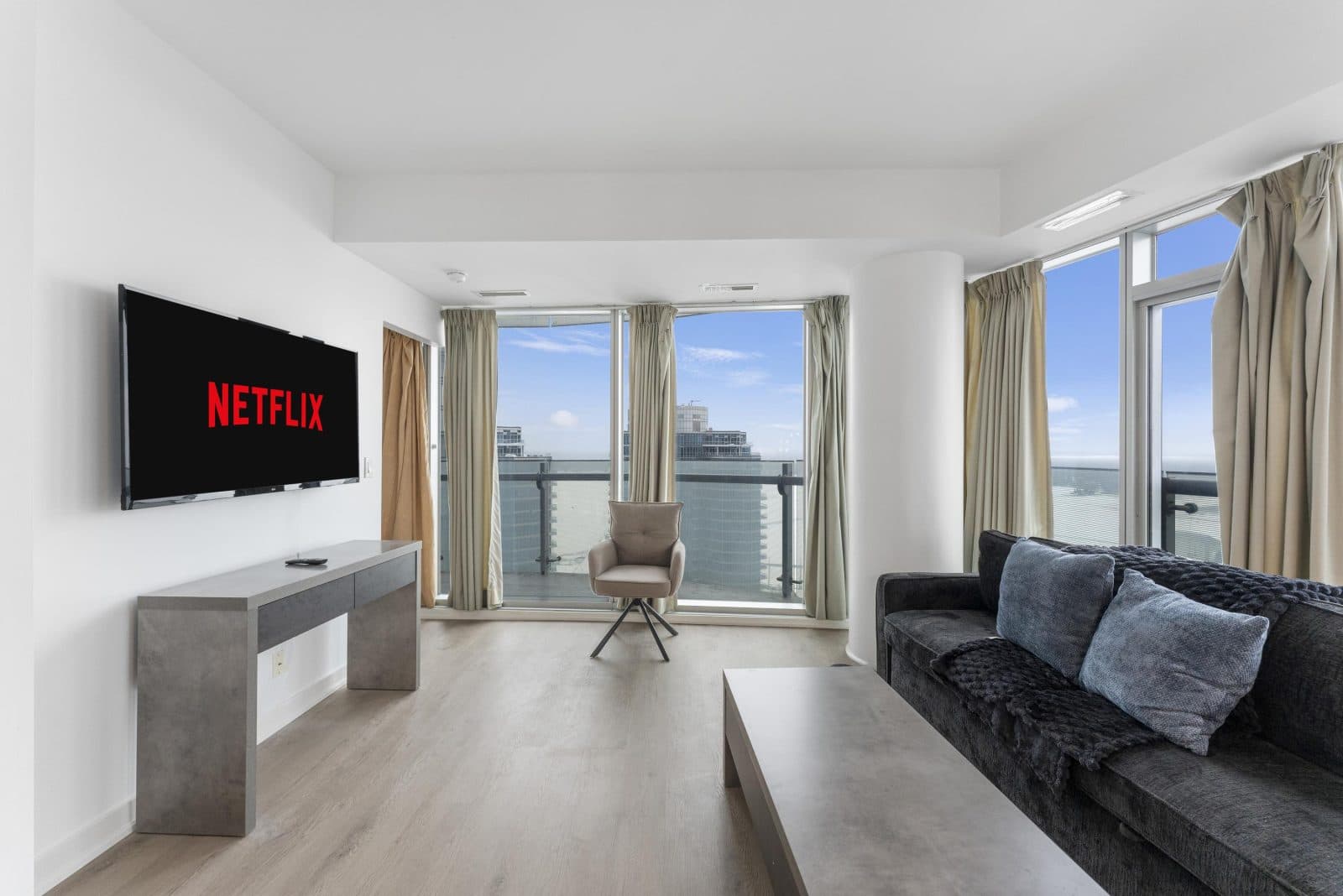 Living room in a York three-bedroom, two-bathroom suite, with a dark sofa, pale floors and tall windows